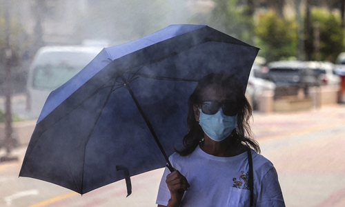 A woman walks with an umbrella underneath sprinklers releasing water vapor in Dubai, UAE on August 25, 2021. Photo: AFP 