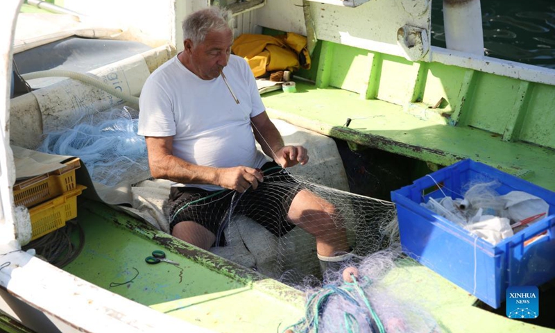 A fisherman weaves a fishing net inside his boat at a fish market of the old port in Marseille, France, Sept. 6, 2021. (Photo: Xinhua)