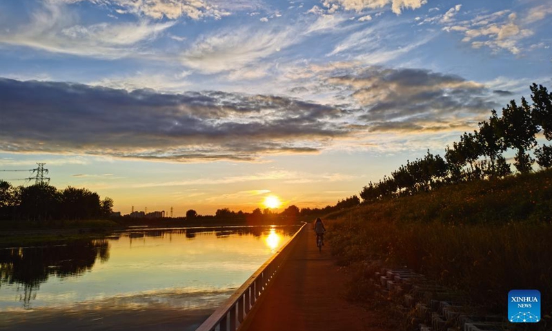 Photo taken with a mobile phone shows a girl riding bike along the Liangshui River at sunset in Tongzhou District of Beijing, capital of China, Sept. 20, 2021.Photo:Xinhua