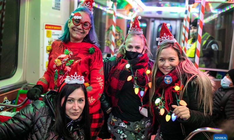 People pose for a photo in the Holiday Train on the Blue Line in Chicago, the United States, Dec. 18, 2021. The year of 2021 marks the 30th anniversary for the Holiday Train service by Chicago Transit Authority. (Photo by Joel Lerner/Xinhua)