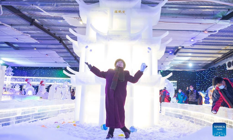 A visitor poses in front of an ice sculpture in the shape of Yellow Crane Tower, or Huanghelou, a landmark of the city of Wuhan, at an ice and snow art festival in Wuhan, capital of central China's Hubei Province, Dec. 21, 2021. As part of the 8th National Public Ice and Snow Season, the ice and snow art festival kicked off here on Tuesday.(Photo: Xinhua)