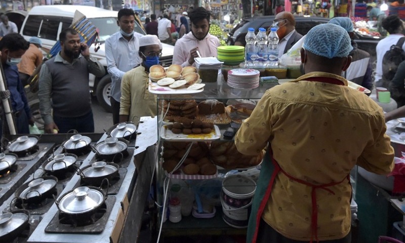 People gather at a roadside stall to eat winter cakes known as Pitha in Dhaka, Bangladesh, Dec. 20, 2021.(Photo: Xinhua)