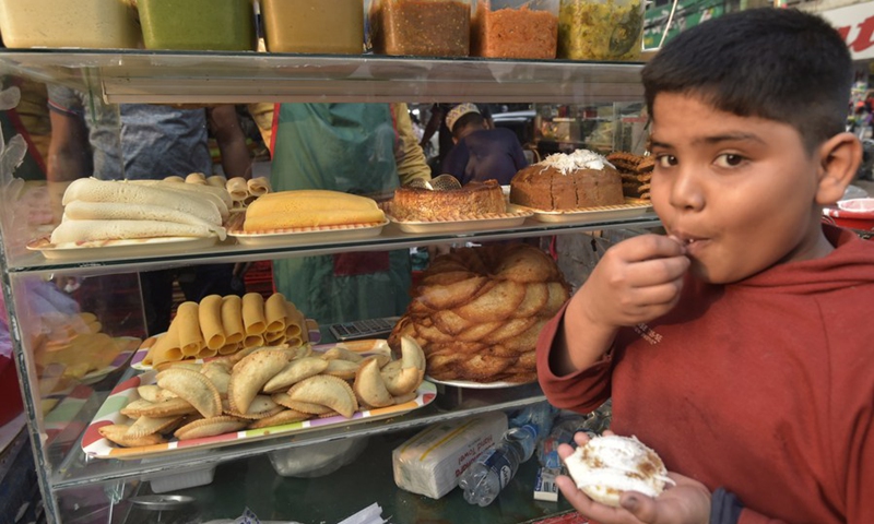 A child eats winter cakes known as Pitha at a roadside stall in Dhaka, Bangladesh, Dec. 20, 2021.(Photo: Xinhua)