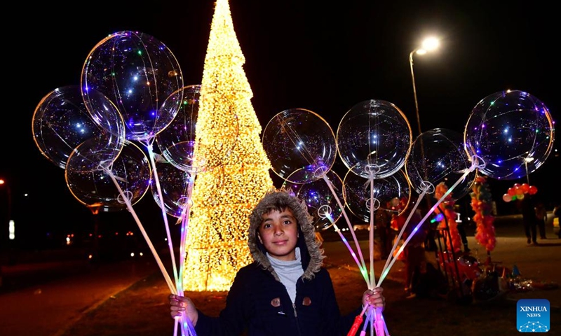 A boy holding balloons poses for photos near a Christmas tree in Damascus, Syria, on Dec 29, 2021. Photo:Xinhua