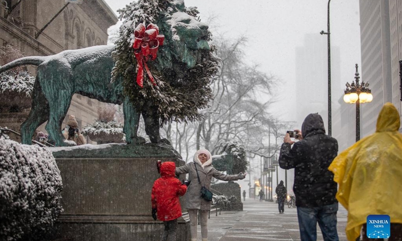 A woman poses in front of the lion at the Art Institute of Chicago in downtown Chicago, the United States, on Jan. 1, 2022. A winter storm hit Chicago on Saturday, with snow accumulation expected to reach 10 to 18 centimeters. (Photo by Vincent D. Johnson/Xinhua)