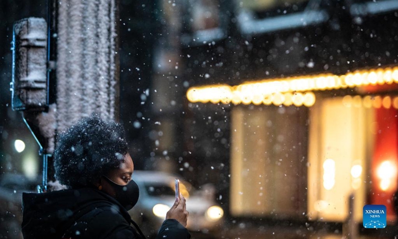 A woman takes photos while waiting for a crosswalk signal in downtown Chicago, the United States, on Jan. 1, 2022. A winter storm hit Chicago on Saturday, with snow accumulation expected to reach 10 to 18 centimeters. (Photo by Vincent D. Johnson/Xinhua)