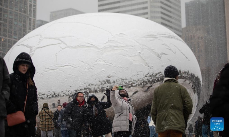 People pose for photos in front of the Cloud Gate sculpture in downtown Chicago, the United States, on Jan. 1, 2022. A winter storm hit Chicago on Saturday, with snow accumulation expected to reach 10 to 18 centimeters. (Photo by Vincent D. Johnson/Xinhua)