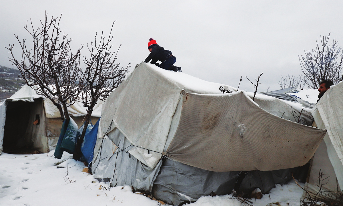 A young Syrian boy clears the snow covering a tent at a camp for internally displaced people, near the city of Jisr al-Shugur on the border with Turkey, in the Idlib governorate of northwestern Syria, on January 23, 2022, as winter storms hit the area. Photo: AFP