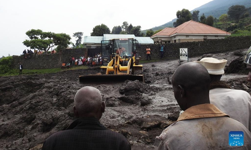 People look at a bulldozer clearing a road blocked by mudslides at Bunagana village in Kisoro district, southwestern Uganda, on Jan. 25, 2022. The death toll from heavy flooding following torrential rains in Kisoro has risen to nine, a humanitarian relief agency said Tuesday.(Photo: Xinhua)