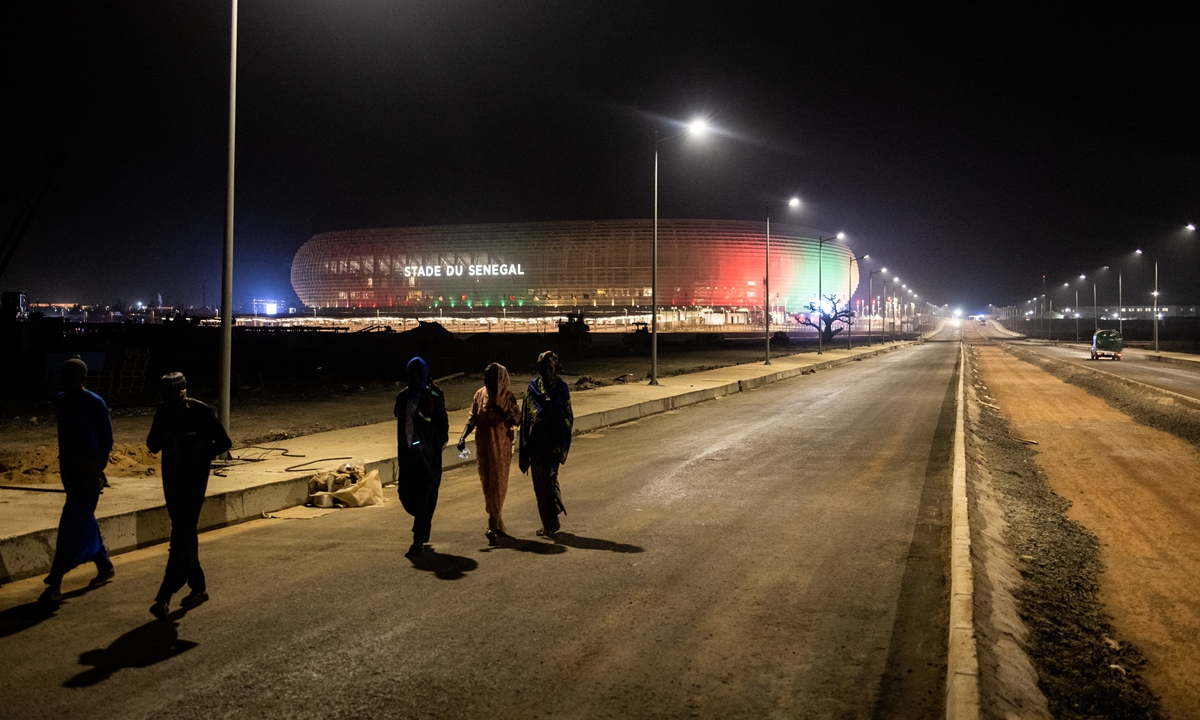 People walk past the new Senegalese Olympic stadium, ahead of its inauguration in Diamniadio on February 22, 2022. The stadium will be a multi-purpose stadium, which can host soccer, rugby and athletics. It will be the national stadium of the Senegal national soccer team, and a venue for the 2026 Youth Olympic Games. Photo: AFP