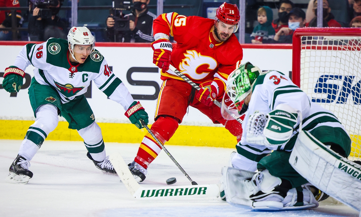 Calgary Flames' Brad Richardson (center) and Minnesota Wild's Jared Spurgeon (left) battle for the puck in Calgary, Canada on February 26, 2022. Photo: AFP