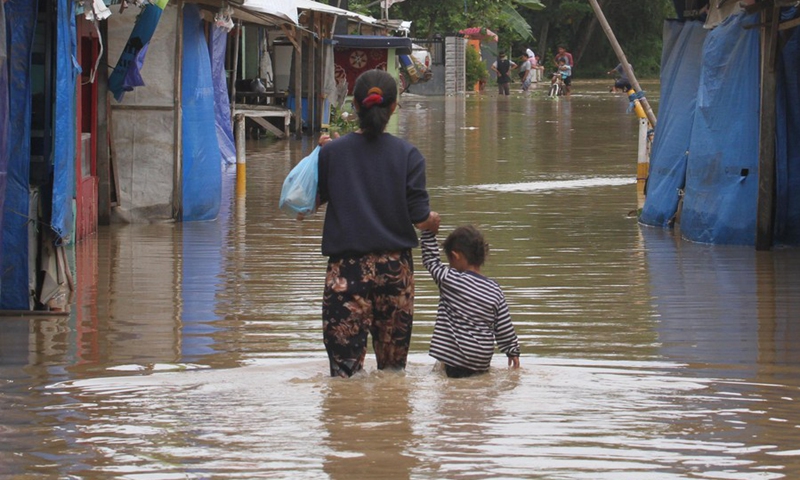 A woman and her child walk through floodwater in Sukajaya village of Serang, Banten Province, Indonesia, March 2, 2022.(Photo: Xinhua)