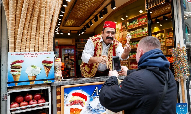 An ice cream vendor presents ice cream to his customer in Istanbul, Turkey, March 5, 2022. The streets of Turkey's biggest city Istanbul are filled with a variety of delicious foods, desserts, drinks, attracting Turkish people and tourists.(Photo: Xinhua)