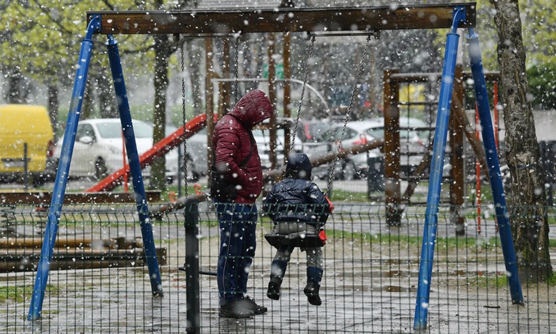 A boy accompanied by his father plays on a swing during a snowfall in Zagreb, Croatia, April 2, 2022.Photo:Xinhua