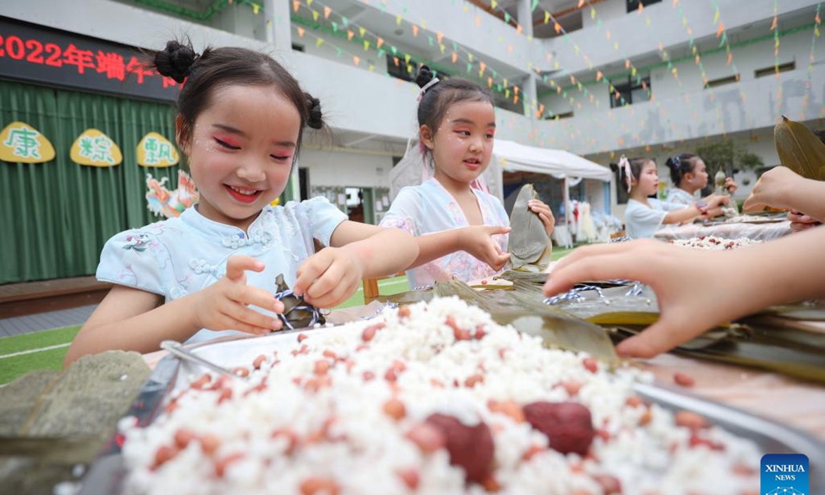 Children learn to make Zongzi, a pyramid-shaped dumpling made of glutinous rice wrapped in bamboo or reed leaves, on the eve of the Dragon Boat Festival in Daying County of Suining City, southwest China's Sichuan Province, June 2, 2022. The Dragon Boat Festival will fall on June 3 this year. (Photo by Liu Changsong/Xinhua)