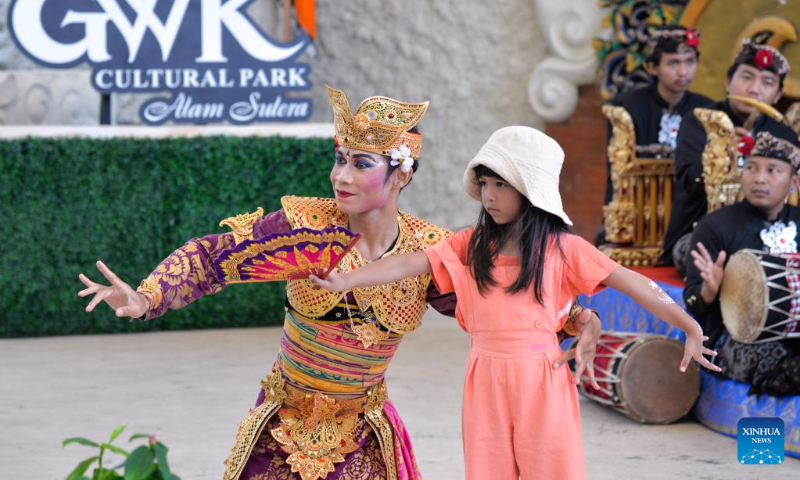 A dancer interacts with a girl during a traditional Balinese dance performance in a cultural park in Bali, Indonesia, July 10, 2022. (Xinhua/Xu Qin)