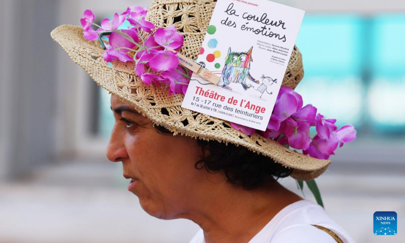 An artist walks on the street to promote her drama by clipping a leaflet on her hat during the 76th Festival d'Avignon in Avignon, France, July 19, 2022. (Xinhua/Gao Jing)