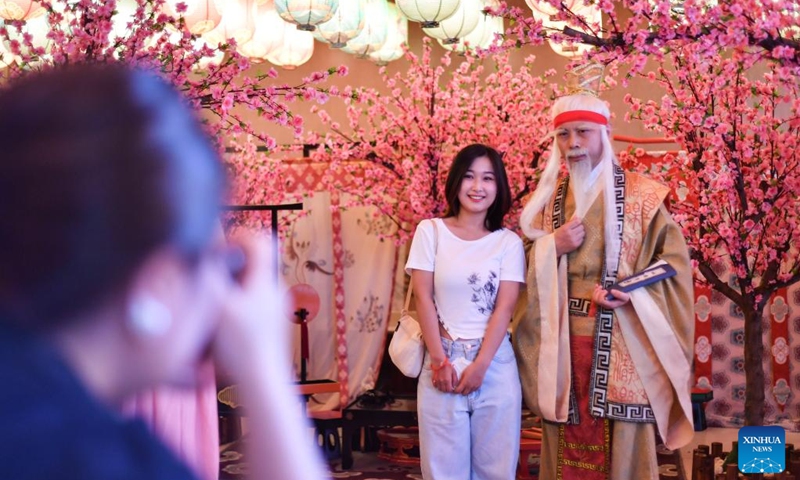 A tourist poses for a photo with a performer of Yuelao, a god of marriage and love in Chinese mythology, on the occasion of Qixi Festival in Qujiang New District in Xi'an, northwest China's Shaanxi Province, Aug. 4, 2022. The Qixi Festival, or Chinese Valentine's Day, falls on Aug. 4 this year. (Xinhua/Zhang Bowen)