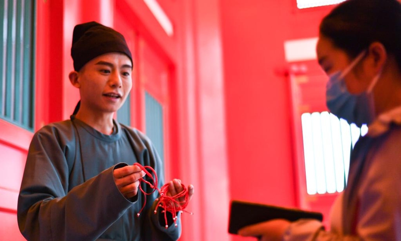 A performer distributes red ropes to tourists on the occasion of Qixi Festival in Qujiang New District in Xi'an, northwest China's Shaanxi Province, Aug. 4, 2022. The Qixi Festival, or Chinese Valentine's Day, falls on Aug. 4 this year. (Xinhua/Zhang Bowen)