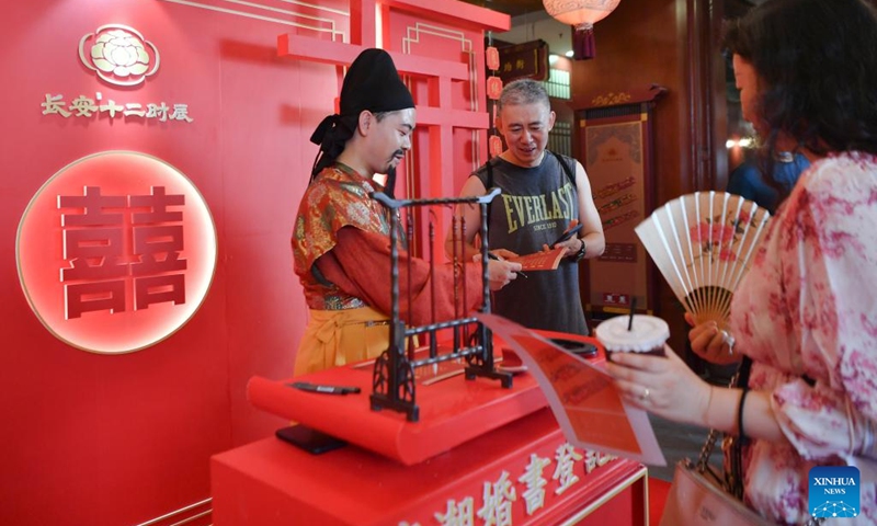 A performer gives a marriage certificate to a tourist on the occasion of Qixi Festival in Qujiang New District in Xi'an, northwest China's Shaanxi Province, Aug. 4, 2022. The Qixi Festival, or Chinese Valentine's Day, falls on Aug. 4 this year. (Xinhua/Zhang Bowen)