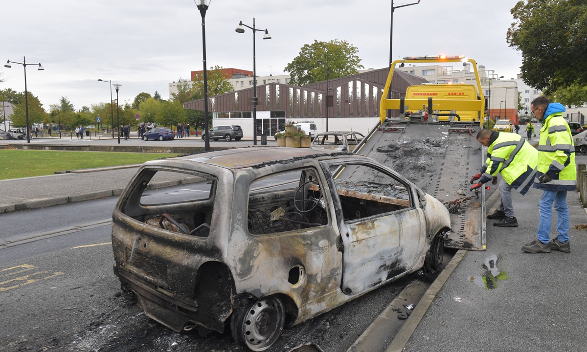 Workers remove a burnt car from the street after overnight violence in the Perseigne neighborhood of Alencon, northwestern France, on September 28, 2022. Police officers were targeted by fireworks and around 20 vehicles were burned in the night of September 27 in Alencon, according to the public prosecutor's office of the Normandy city. Photo: AFP