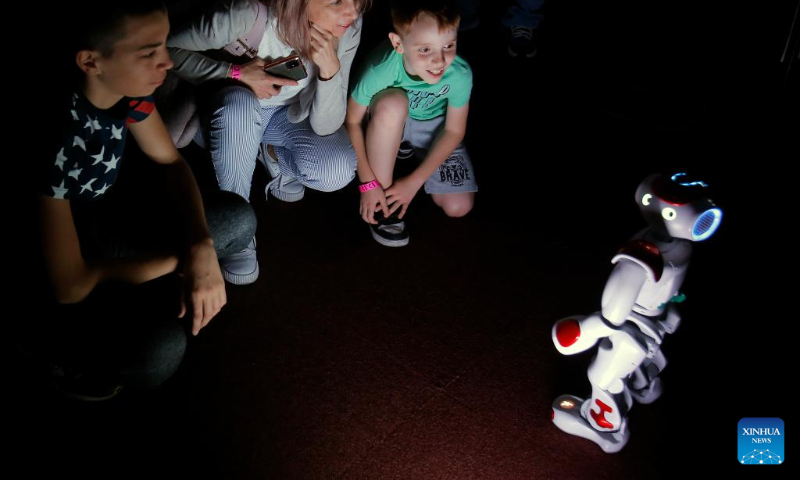 People interact with a small intelligent robot while visiting the 3rd edition of the new media art festival RADAR in Bucharest, capital of Romania, Oct. 16, 2022. (Photo by Cristian Cristel/Xinhua)