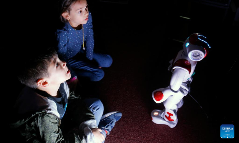 Children interact with a small intelligent robot while visiting the 3rd edition of the new media art festival RADAR in Bucharest, capital of Romania, Oct. 16, 2022. (Photo by Cristian Cristel/Xinhua)