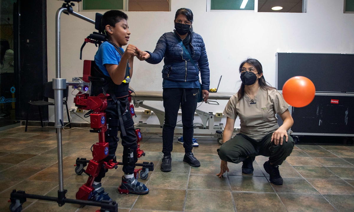 David Zabala, an 8-year-old boy with cerebral palsy, is assisted by a physical therapist and his mother, Guadalupe Cardozo Ruiz (C), during a rehabilitation session with the robotic exoskeleton Atlas 2030 at the Association for People with Cerebral Palsy (APAC) in Mexico City on October 18, 2022.  Photo: VCG