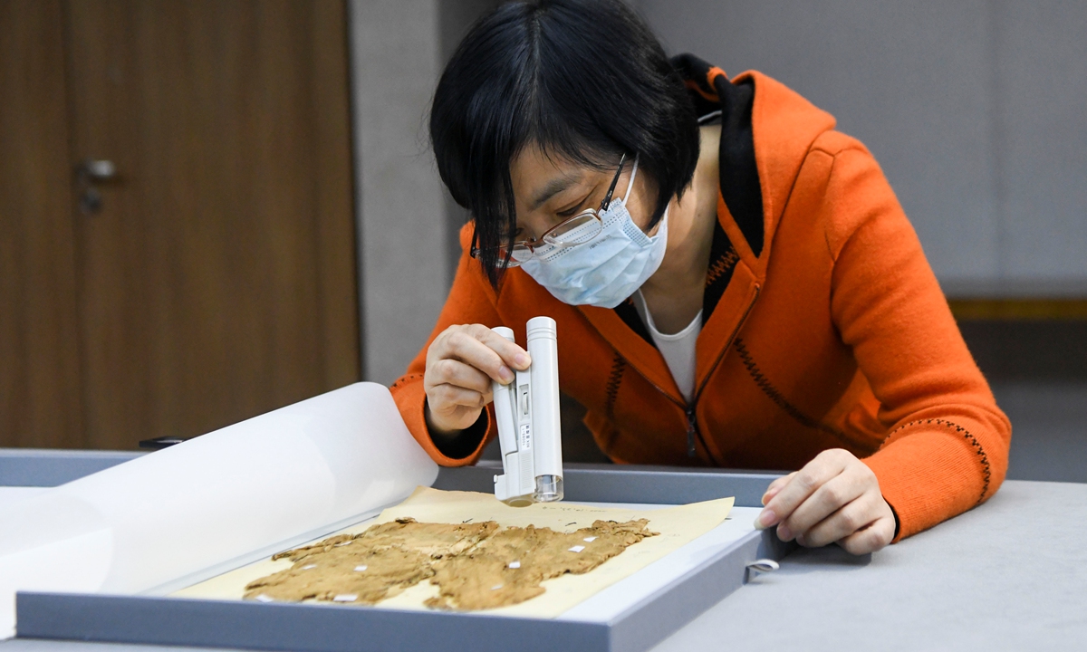 = A researcher at the Hunan Museum in Changsha, Central China's Hunan Province checks auspicious phrases on silk fabrics on November 2, 2022. Researchers excavated a silk garment from?the Mawangdui Tomb that was inscribed with the phrase peace and happiness, longevity and infinite life, the earliest inscription found on a silk fabric so far.?Photo: IC