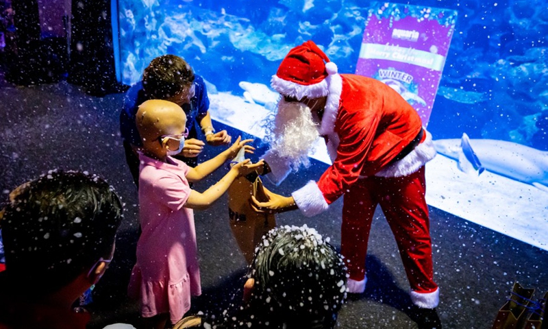 A Wish Child (L) receives a gift from Santa Claus during the Winter Wondersea event at Aquaria KLCC aquarium in Kuala Lumpur, Malaysia, Nov. 30, 2022.(Photo: Xinhua)