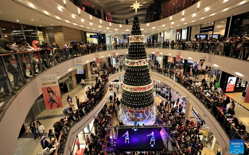 People gather around a giant Christmas tree to watch holiday celebration performances at a shopping mall in Beirut, Lebanon, on Dec. 24, 2022. (Xinhua/Liu Zongya)