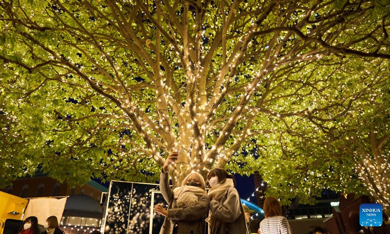 People take selfies under a tree with Christmas lights at the Ebisu Garden Place in Ebisu, Tokyo, Japan, Dec. 25, 2022. (Xinhua/Zhang Xiaoyu)