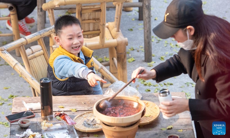 Tourists taste local food at Shancheng Alley of the Jiefangbei business district in Chongqing, southwest China, on Dec. 24, 2022. (Xinhua/Tang Yi)