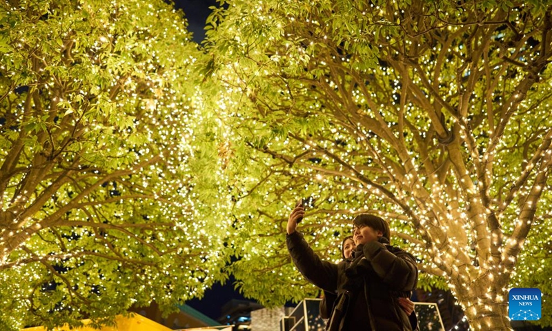 People take selfies under trees with Christmas lights at the Ebisu Garden Place in Ebisu, Tokyo, Japan, Dec. 25, 2022. (Xinhua/Zhang Xiaoyu)