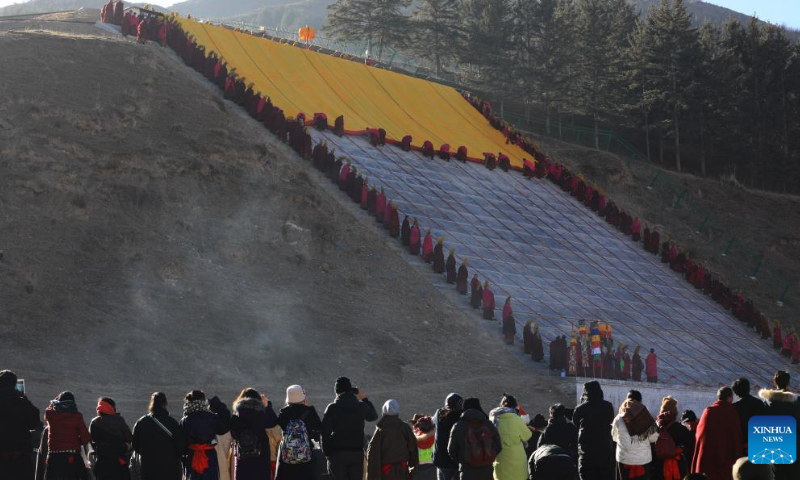 People wait for the unrolling of a huge thangka scroll bearing the image of the Buddha during the sunning of the Buddha ceremony at the Labrang Monastery in Xiahe County, northwest China's Gansu Province, Feb. 3, 2023. 