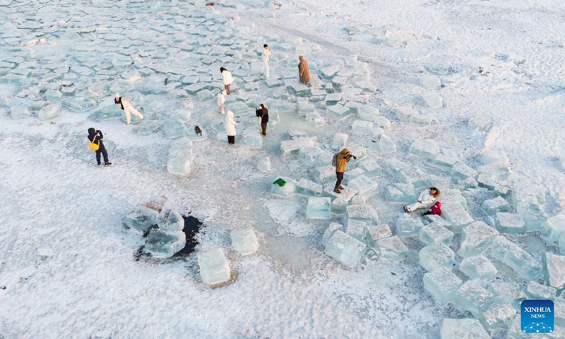 This aerial photo taken on Feb. 1, 2023 shows people posing for photos on ice cubes at a section of Songhuajiang River in Harbin, northeast China's Heilongjiang Province. This section of frozen river used to be the source of natural ice for installations at the Harbin Ice and Snow World. Some giant ice cubes were cut out but left there unused.(Photo: Xinhua)