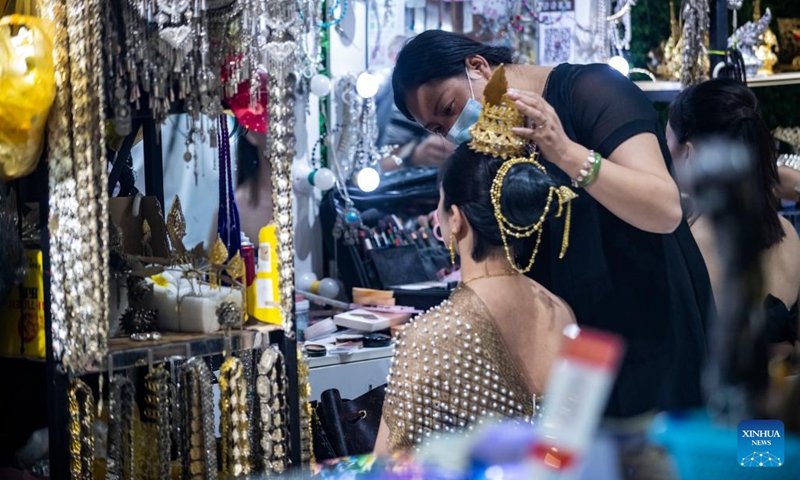 A dresser puts on makeup for a tourist at a night fair in Jinghong City of Xishuangbanna Dai Autonomous Prefecture, southwest China's Yunnan Province, Feb. 12, 2023. The night fair here has attracted a good many tourists, some of whom enjoyed a travel photo service in which photo studios provided traditional costumes and makeup to tourists.(Photo: Xinhua)