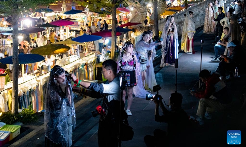 Photographers take photos for tourists at a night fair in Jinghong City of Xishuangbanna Dai Autonomous Prefecture, southwest China's Yunnan Province, Feb. 13, 2023. The night fair here has attracted a good many tourists, some of whom enjoyed a travel photo service in which photo studios provided traditional costumes and makeup to tourists.(Photo: Xinhua)