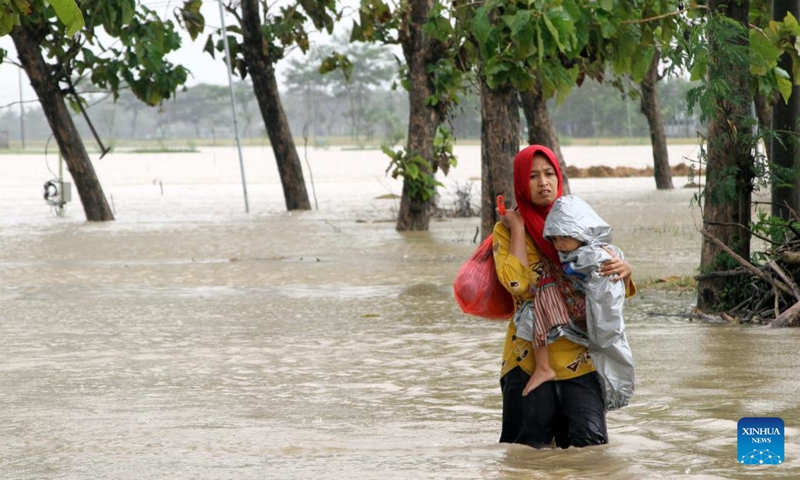 A mother holds her child while wading through flood water after heavy rainfall and overflow of the Bengawan Solo River in Sragen, Central Java, Indonesia, March 2, 2023.(Photo: Xinhua)