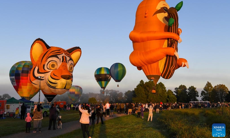 People watch hot balloons flying above the sky during the 5-day Balloons Over Waikato Festival in Hamilton, New Zealand, March 15, 2023.(Photo: Xinhua)