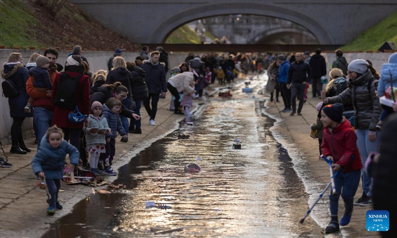 People look at miniature boats floating down a river in Ljubljana, Slovenia on March 11, 2023. According to the Slovenian old calendar, March 12 marks the start of Spring. It is a local tradition to send off miniature boats downstream on March 11 to celebrate Spring's arrival. (Photo:Xinhua)