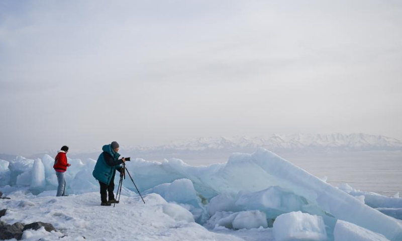 A tourist takes photos of Sayram Lake in Bortala Mongolian Autonomous Prefecture, northwest China's Xinjiang Uygur Autonomous Region, April 6, 2023. The frozen Sayram Lake in Xinjiang has begun to thaw amid rising temperatures. Surrounded by grasslands and the Tianshan Mountains, the lake attracts lots of tourists every day. (Xinhua/Li Xiang)