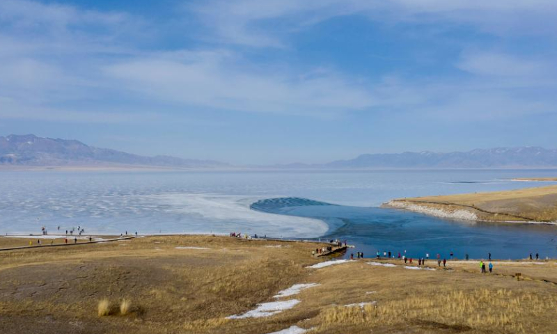 This aerial photo taken on April 6, 2023 shows tourists visiting Sayram Lake in Bortala Mongolian Autonomous Prefecture, northwest China's Xinjiang Uygur Autonomous Region. The frozen Sayram Lake in Xinjiang has begun to thaw amid rising temperatures. Surrounded by grasslands and the Tianshan Mountains, the lake attracts lots of tourists every day. (Xinhua/Yang Zhisen)