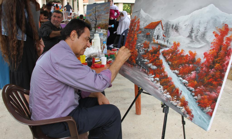 A man creates a painting of rural landscape during the Lebanese Exhibition of Handicrafts and Agricultural Products at Al-Khan Market in Hasbaya, Lebanon, on May 13, 2023. (Photo by Taher Abu Hamdan/Xinhua)