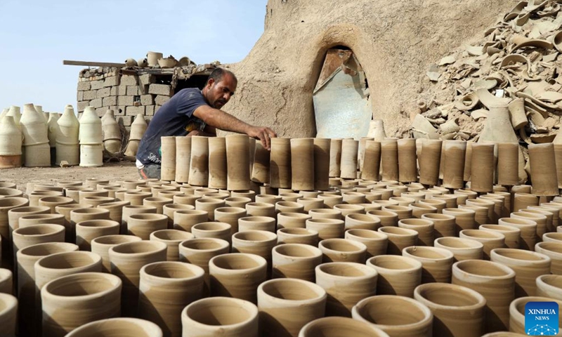 Safaa al-Kawaz, a pottery workshop owner, arranges earthenware in the Nahrawan area near Baghdad, Iraq, May 27, 2023. Pottery-making in Iraq has been an enduring profession which is deeply rooted in the civilizations of Mesopotamia. (Xinhua/Khalil Dawood)