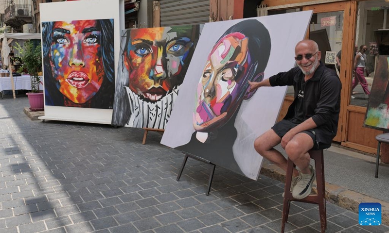 An artist points at his paintings at a street fair in Beirut, Lebanon, on May 21, 2023(Photo: Xinhua)