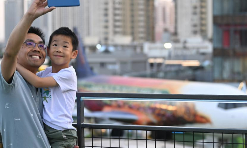 A man holds his child and takes selfies on top of a commercial complex in Heping District, north China's Tianjin, June 2, 2023. Transformed from four vacant buildings, a commercial complex was unveiled in Heping District of Tianjin recently. This commercial complex not only offers people with shopping malls but also leisure spaces such as rooftop parks and pocket parks. The airplane themed bar and other entertainment spaces located on top of the commercial complex gained popularity for the surrounding business area. (Xinhua/Li Ran)