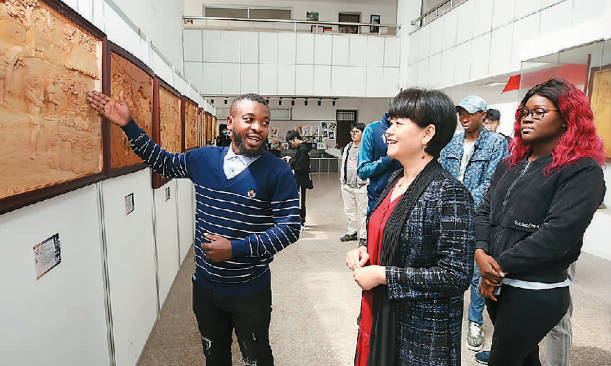 International students from the Republic of the Congo are explaining the creative ideas and the meaning of their Chinese wood carvings to the audience in Chinese. （Photo by Hu Yanghui/People's Daily)