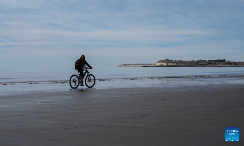 A woman rides a bike on a beach in Puerto Madryn, Argentina, on June 13, 2023. Thousands of whales come to breed and calve here between June and December every year.(Photo: Xinhua)