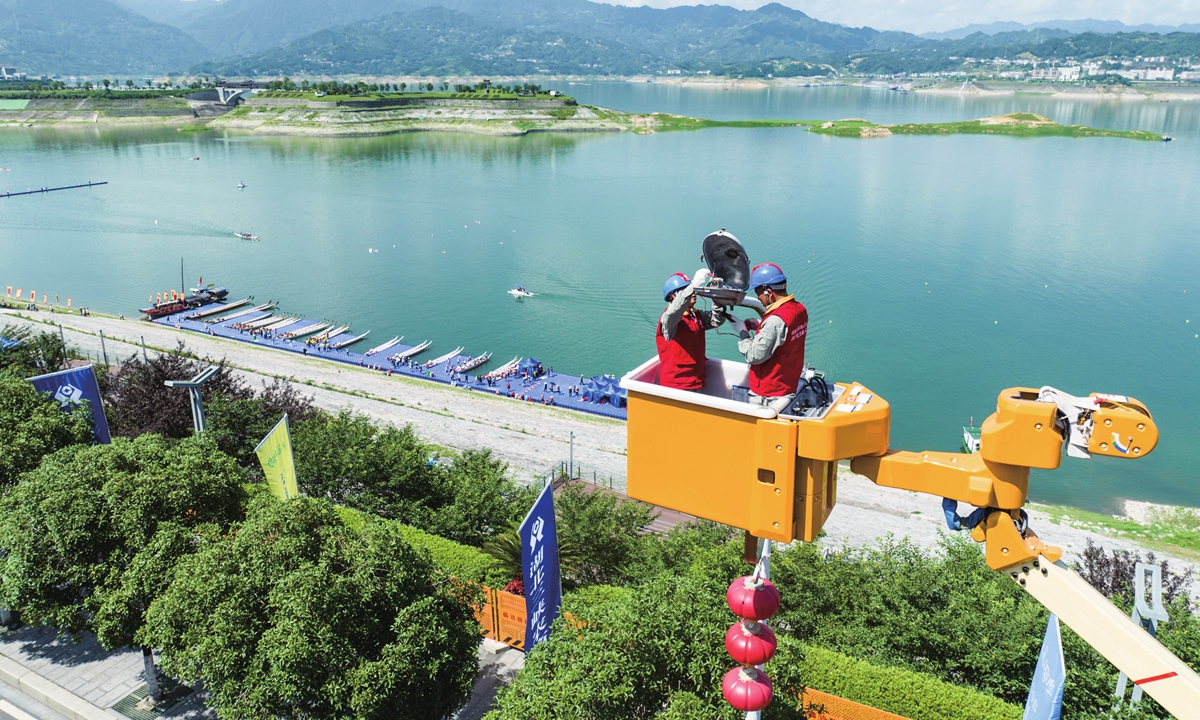 Two workers check the lighting equipment at a site of dragon boat race in Yichang, Central China's Hubei Province on June 20, 2023. The local power supply company deploys emergency power supply vehicles and lays temporary power supply cables, in a bid to ensure the safety and reliability of electricity at the event site. Photo: VCG